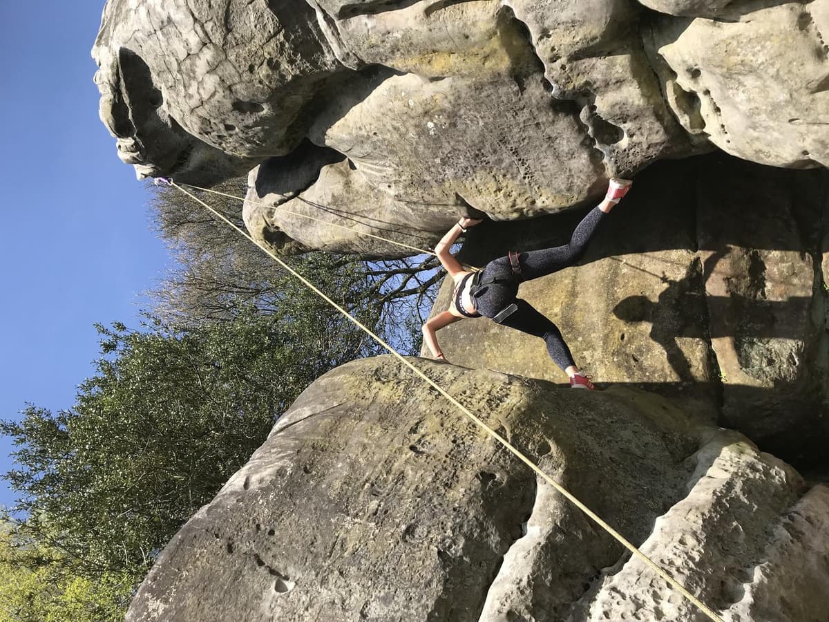A climber working up a rounded boulder on a top rope, the kind of natural rock found on a day of rock climbing near Kathmandu.