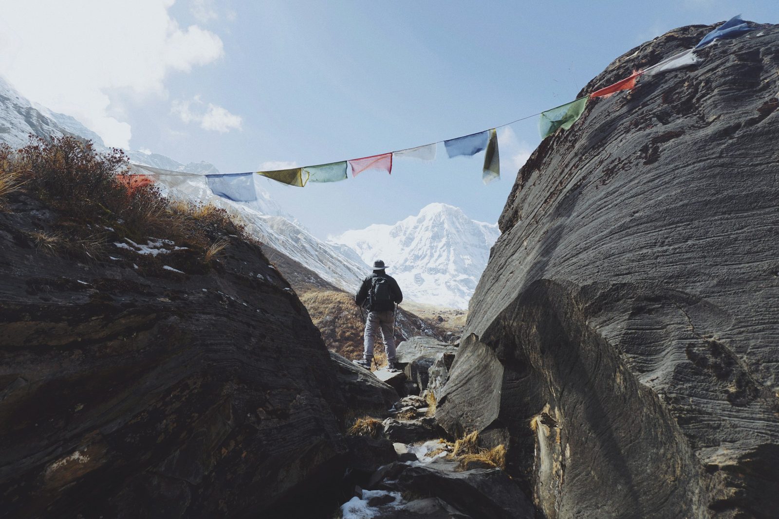 Trekker passing prayer flags between boulders on the Annapurna Base Camp trek