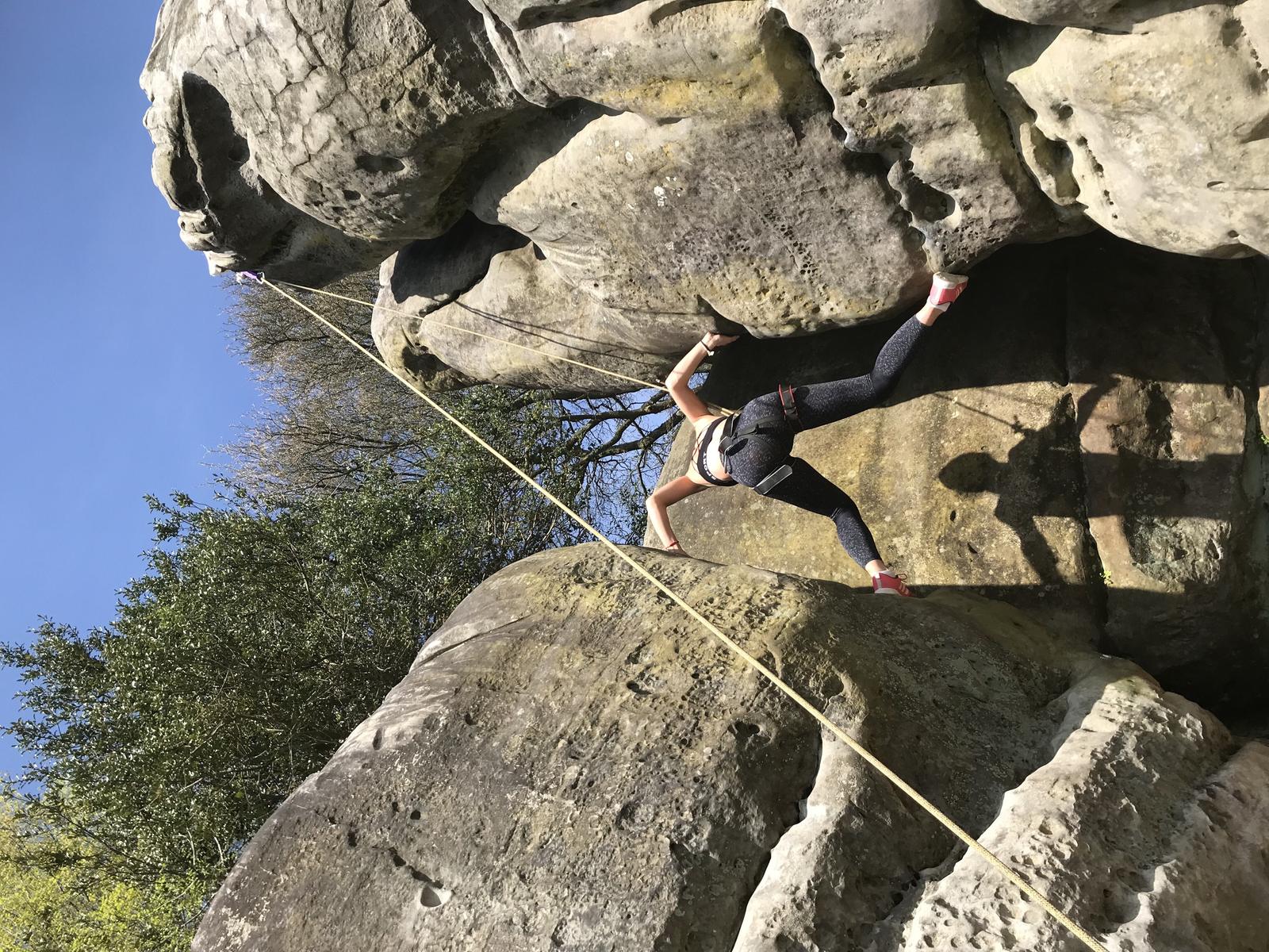 A climber working up a rounded boulder on a top rope, the kind of natural rock found on a day of rock climbing near Kathmandu.