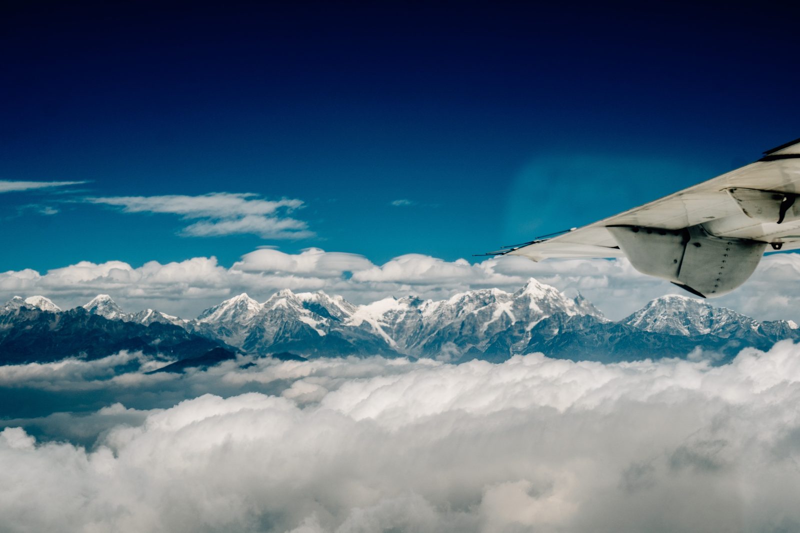 Snow peaks of the Nepal Himalaya above the clouds beside the aircraft wing on the Everest mountain flight.