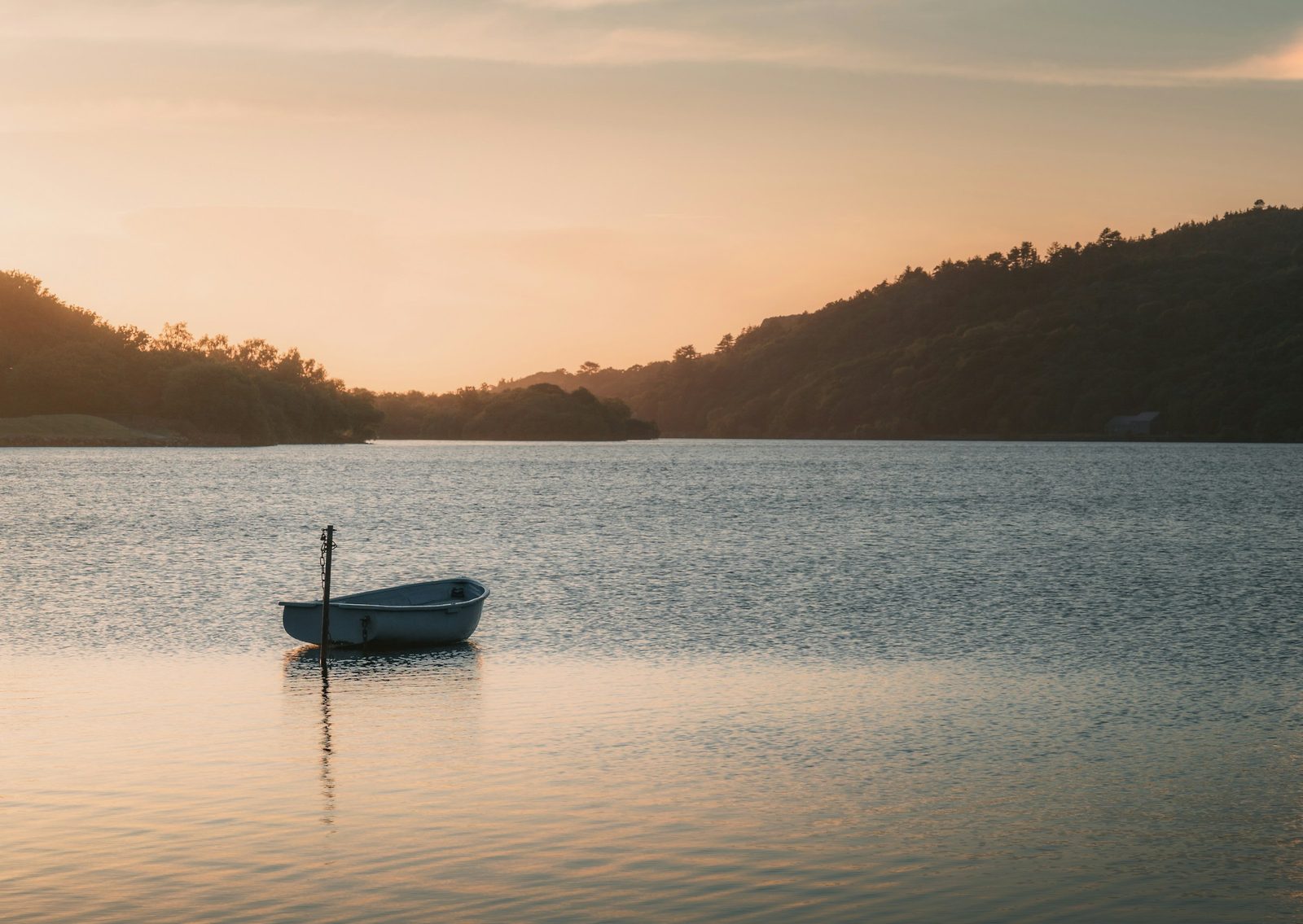 A wooden boat out on calm lake water below the hills on the Kulekhani and Daman tour