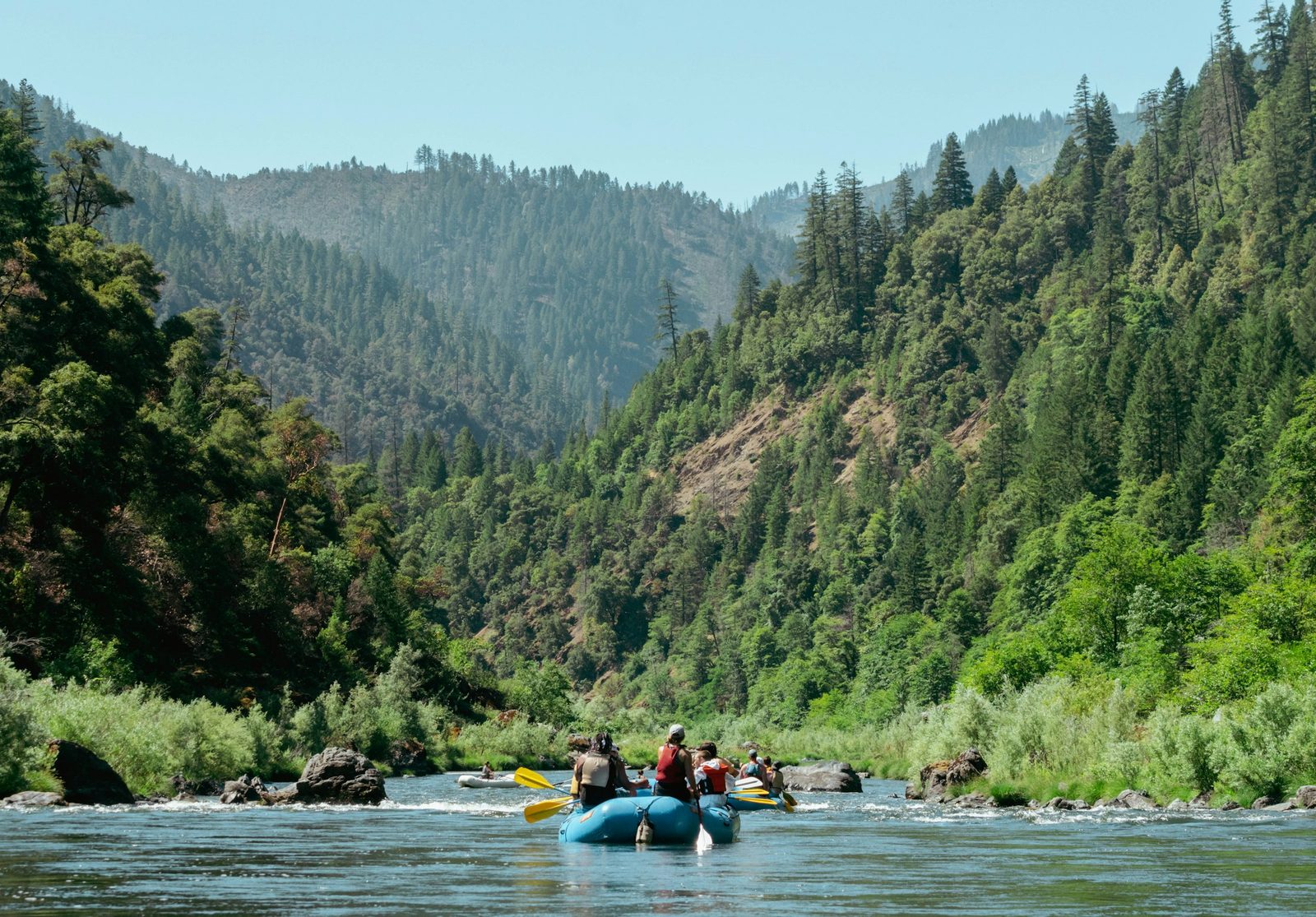 Rafts drifting down a calm green stretch of river through a forested gorge on the Sukute Beach rafting trip